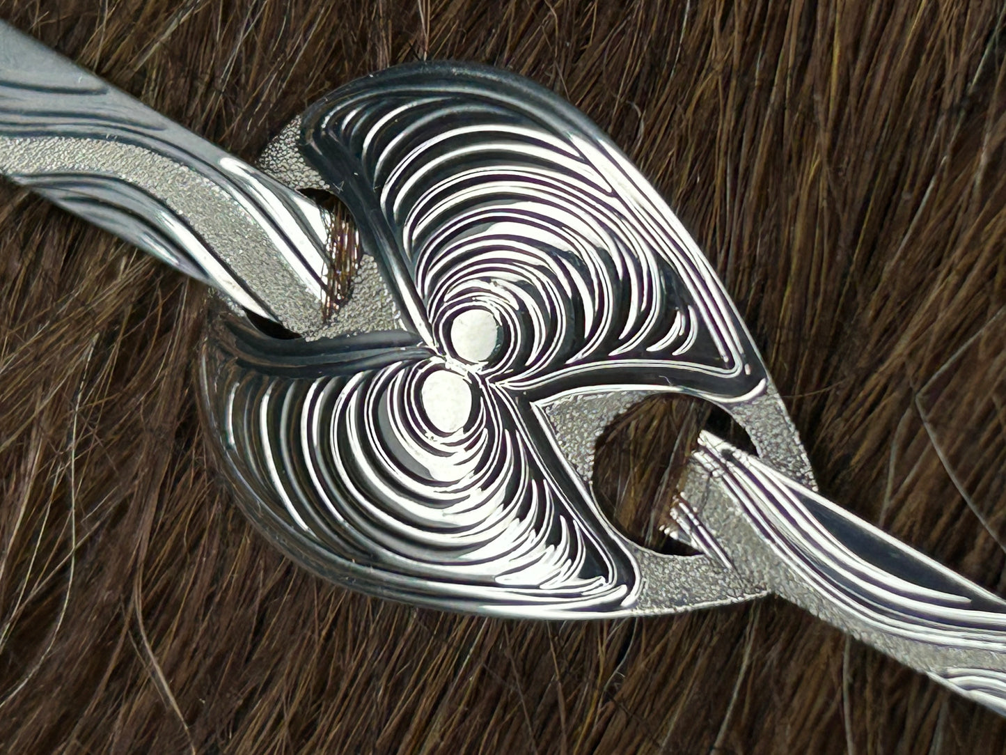 A close up of the butter clam sterling silver hair jewellery designed and engraved by Laura Dutheil. Only a few hairs gathered by the stick to hold hair jewellery in place.