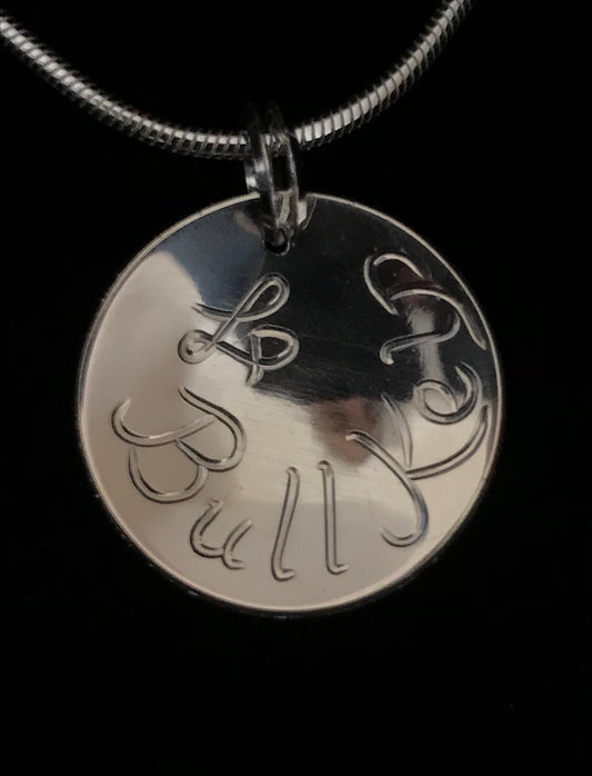 Back of round sterling silver bull kelp pendant with the artist's initials and the words Bull Kelp.